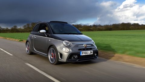 Grey Abarth car driving in a road besides an open field to the right