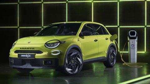 Yellow Abarth 600e being charged in front of a black wall with yellow neon lights