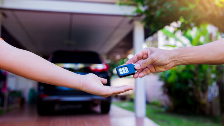 Close up of a hand giving some car keys to another hand, with a car port in the background