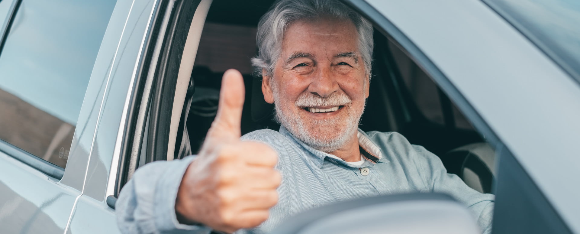 Elderly Male Driver Sticking His Thumb Up Out of the Car Window