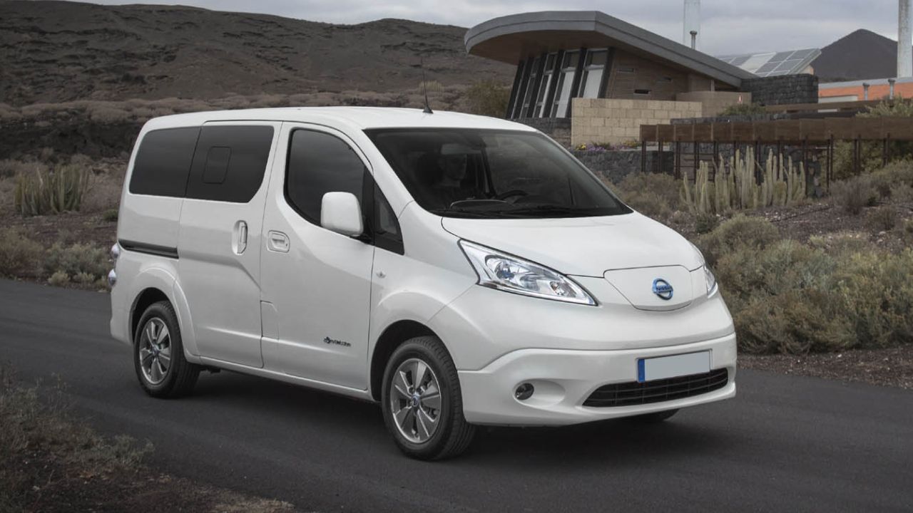White Nissan e-NV200 driving in front of a rural house