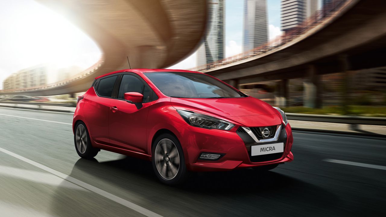 Red Nissan Micra driving under a bridge with huge skyscrapers in the background