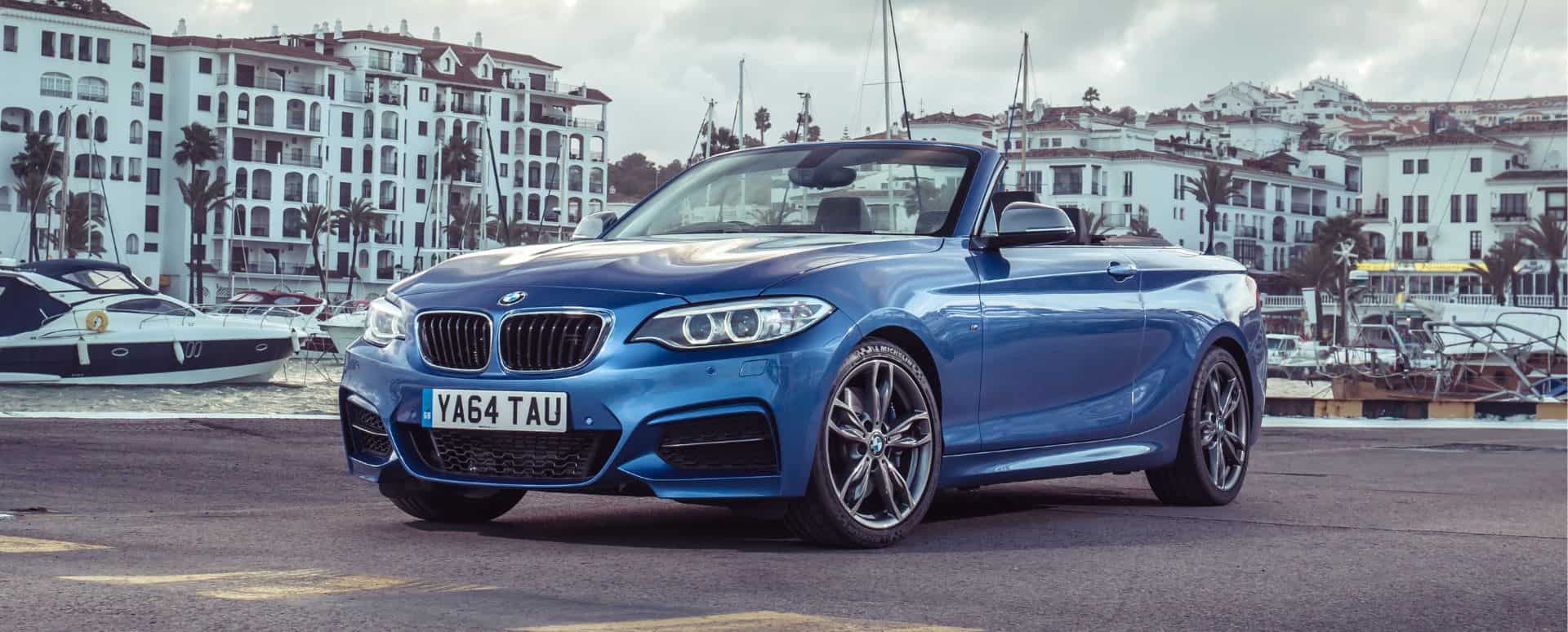 Blue BMW 2 Series Convertible parked in front of the ocean with beach flats in the background