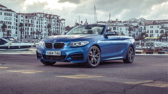 Blue BMW 2 Series Convertible parked in front of the ocean with beach flats in the background