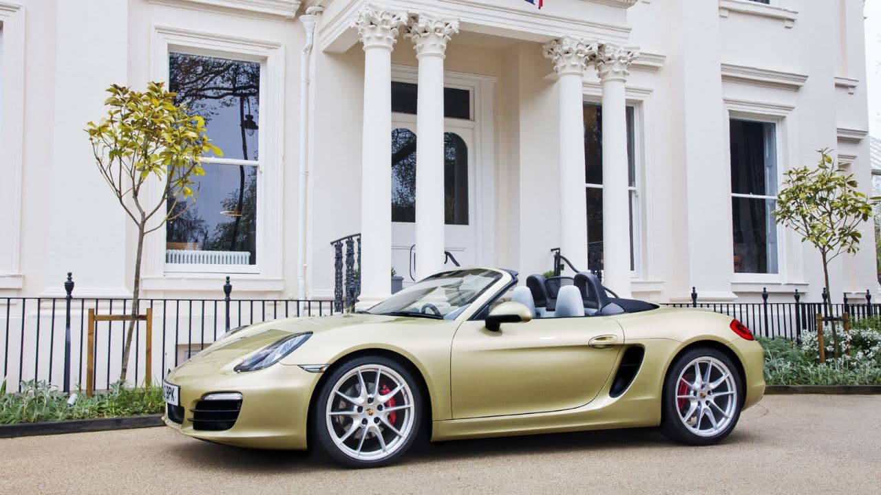 Gold Porsche Boxster parked in front of a white house