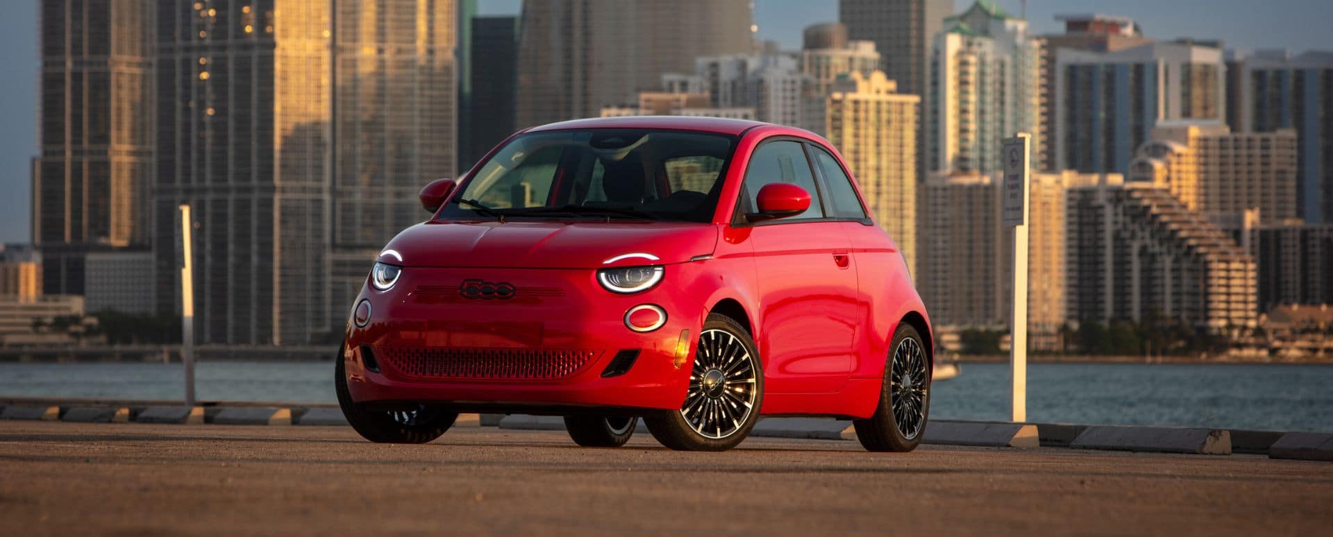 Red Fiat 500e parked in front of a large city skyline