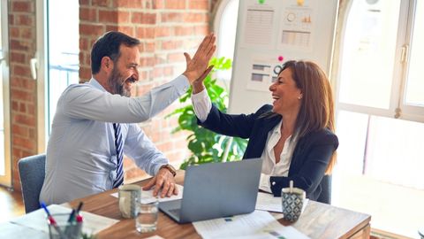 Man in shirt and tie high-fiving a woman wearing a blazer and white shirt