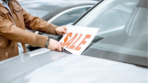 A person wearing a brown jacket puts a sale sign on a vehicle's windshield