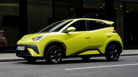 Yellow BYD Dolphin Surf Driving Reflected in Window of Building