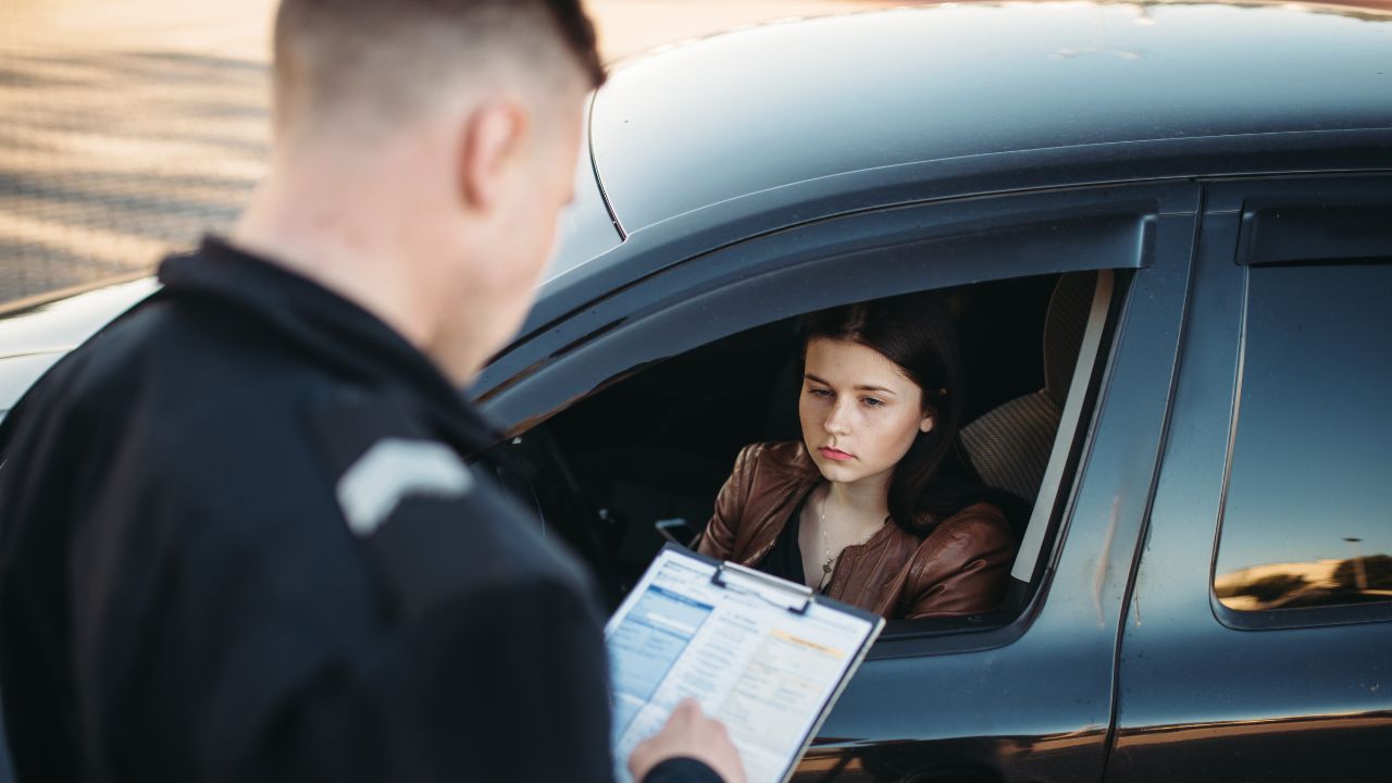 Police officer issuing a ticket to woman who is sitting inside of her car