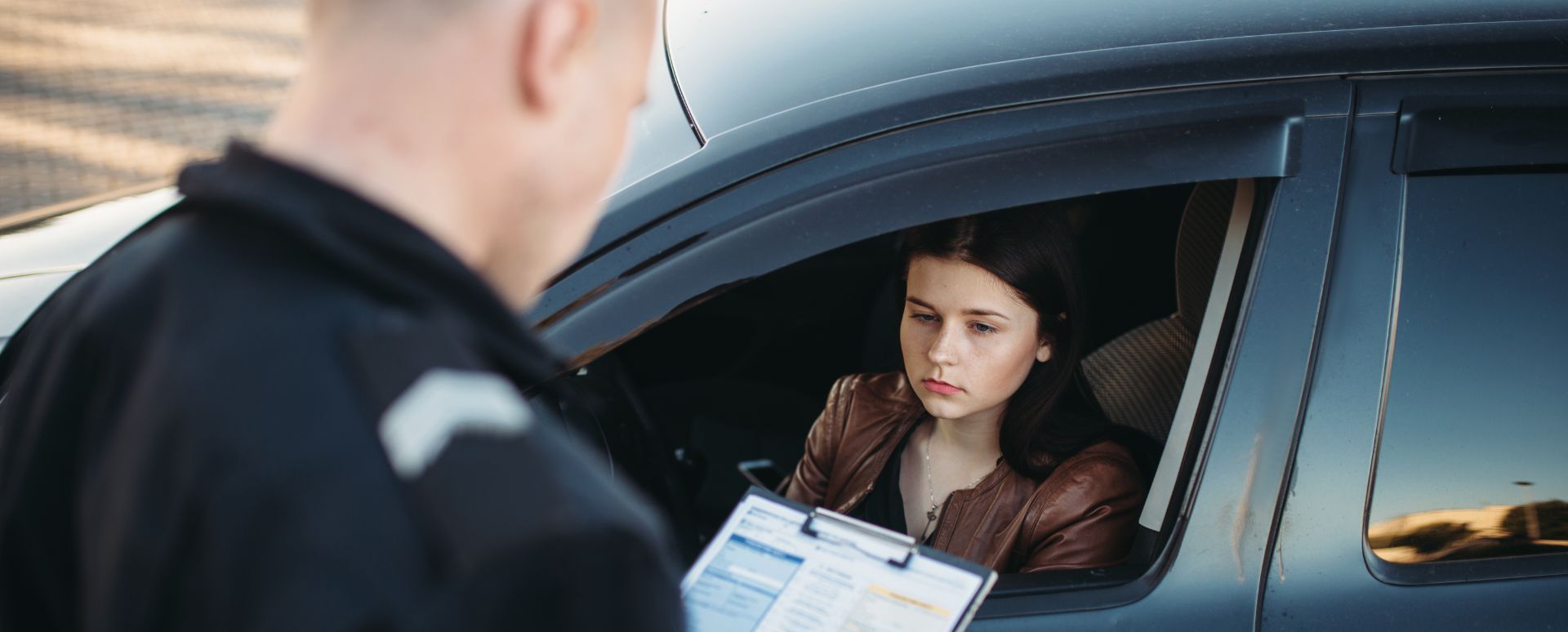 Police officer issuing a ticket to woman who is sitting inside of her car
