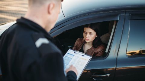 Police officer issuing a ticket to woman who is sitting inside of her car