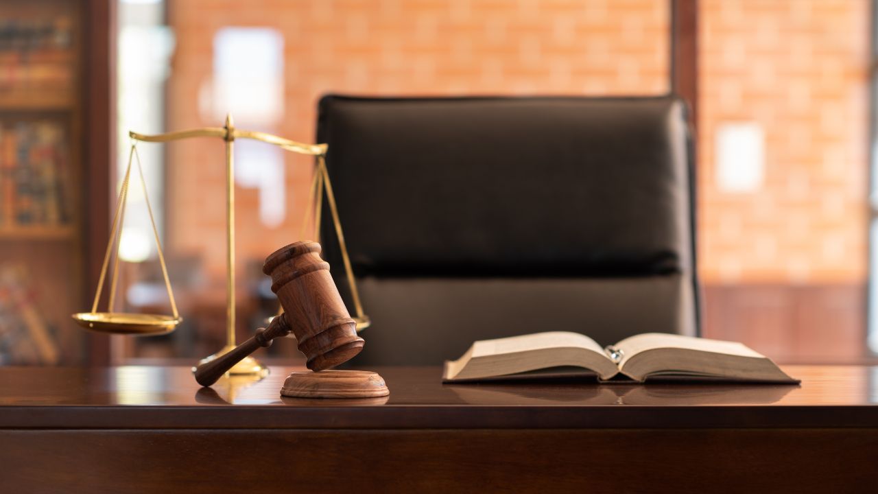Scales and a gavel besides a book on a dark wooden table in a law office