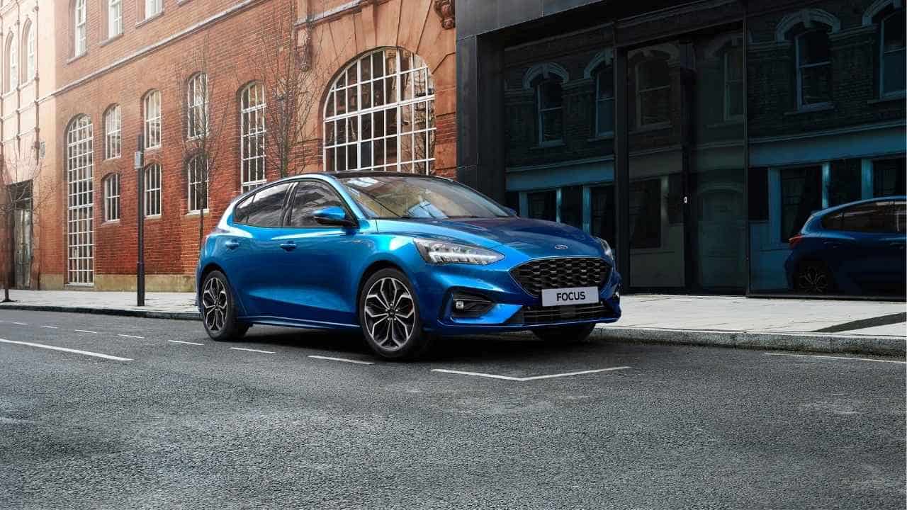 Blue Ford Focus parked in front of a red brick large building and a glass wall building