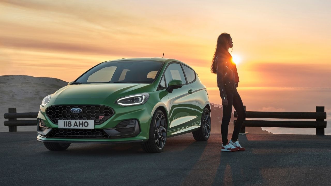 Green Ford Focus parked in a hill with an overview to the ocean. A woman is parked to its side.