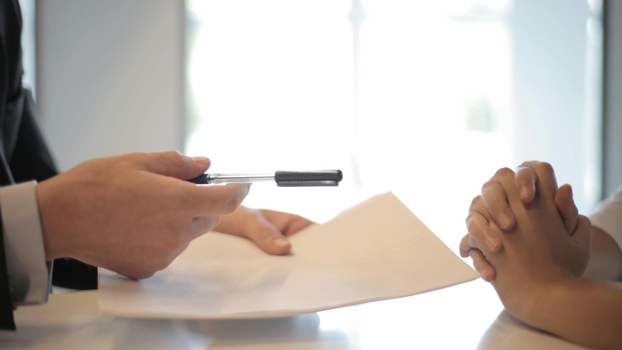 Man handing a pen to a woman who's sitting across the table from him