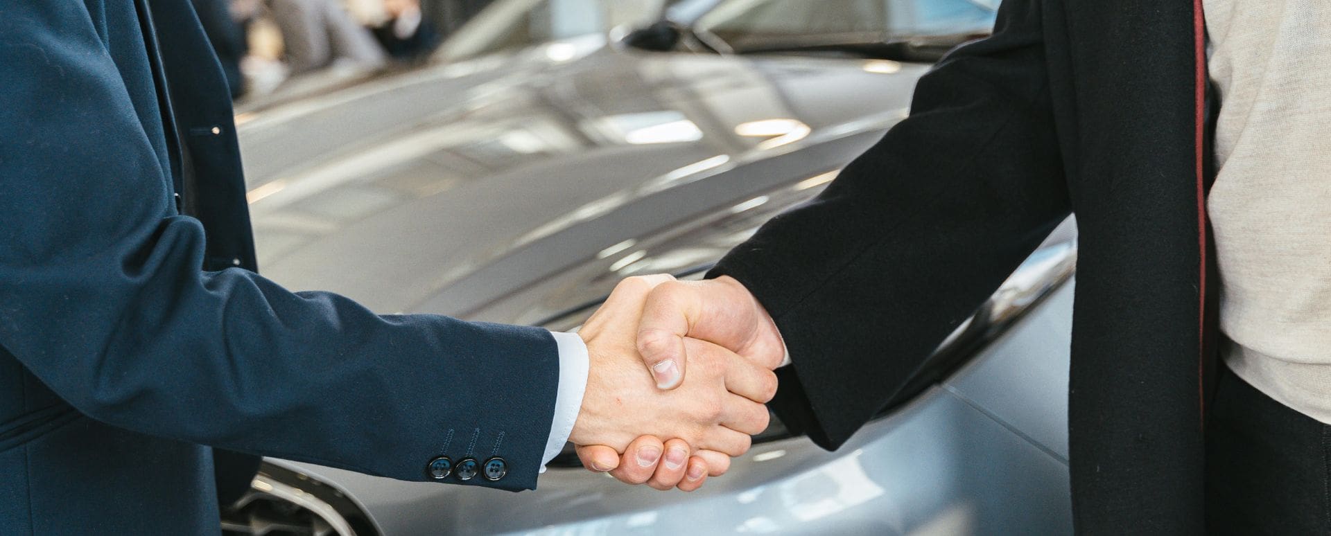 Two men shaking hands in front of a silver car