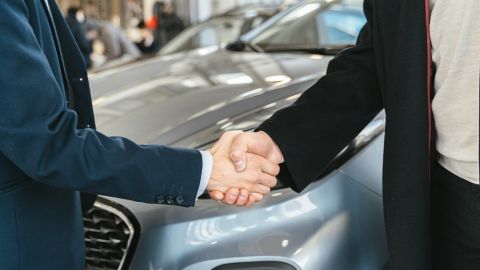 Two men shaking hands in front of a silver car