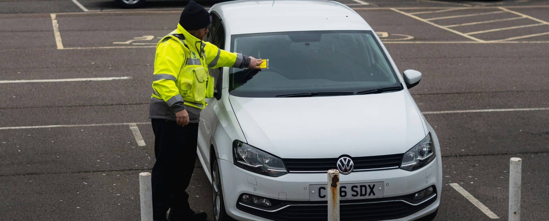 Police officer placing a parking ticket on to a white vehicle's windscreen