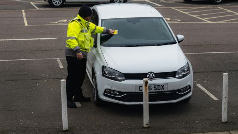 Police officer placing a parking ticket on to a white vehicle's windscreen