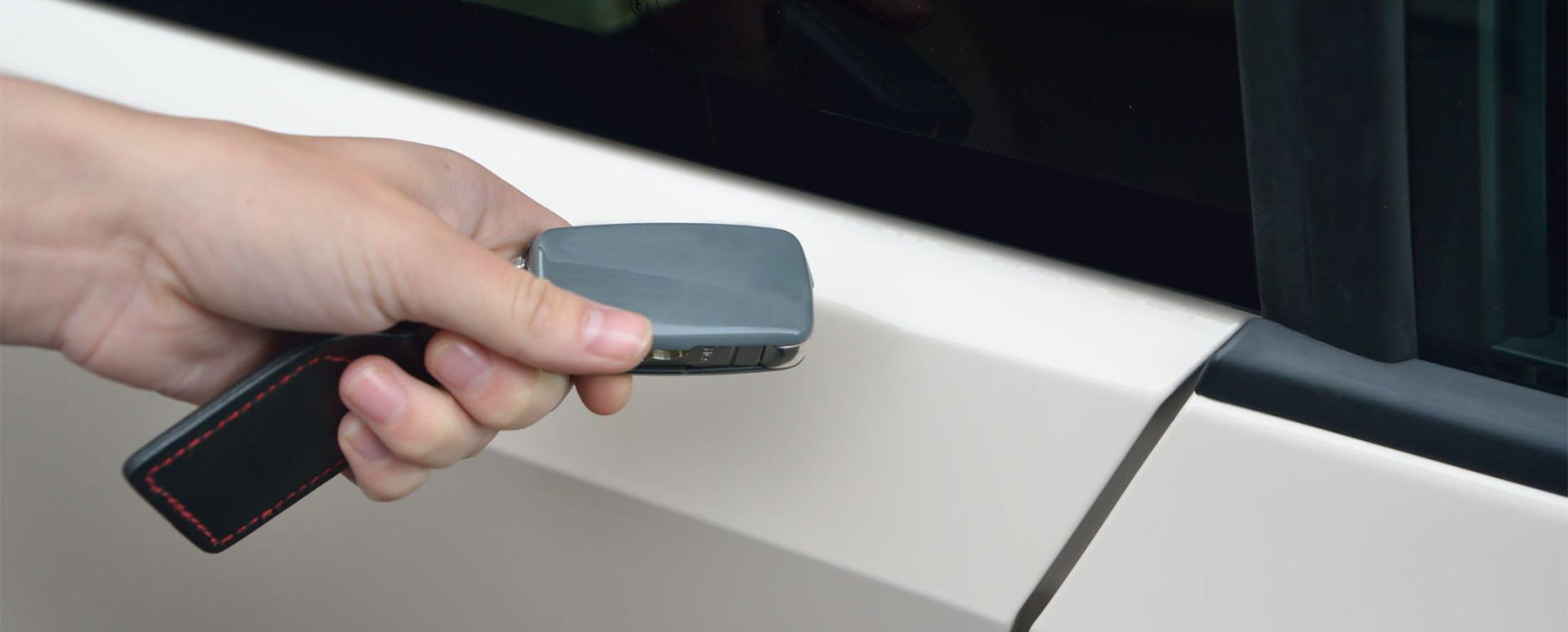 Close up of someone holding a grey fob next to a white car