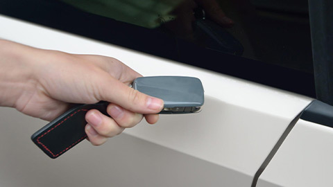 Close up of someone holding a grey fob next to a white car