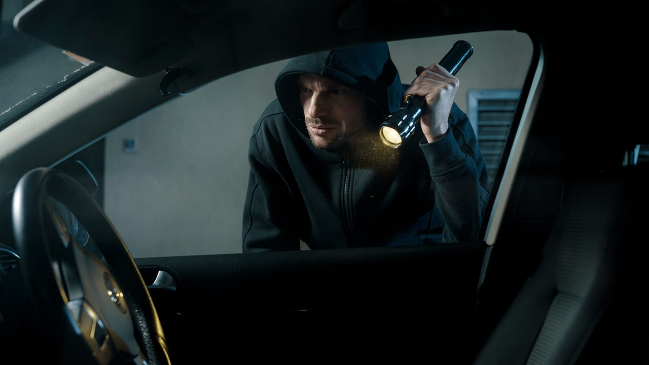 Car thief peeking through a car's window with a torch