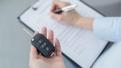Man holding a car key on his left hand and signing a contract with his right hand