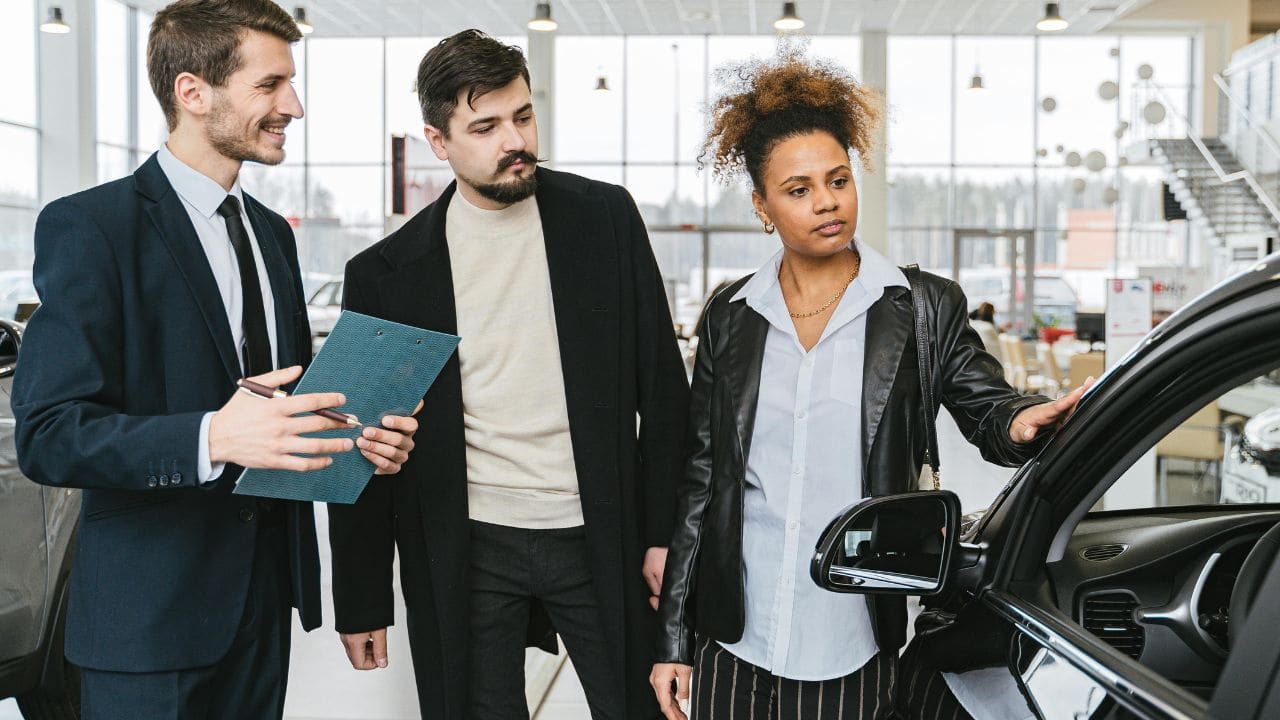 Two men and a woman standing in front of a car whilst looking at it