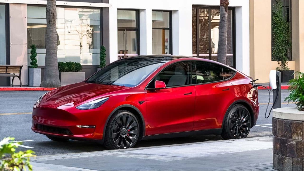 Red Tesla Model Y being charged in front of a glass building