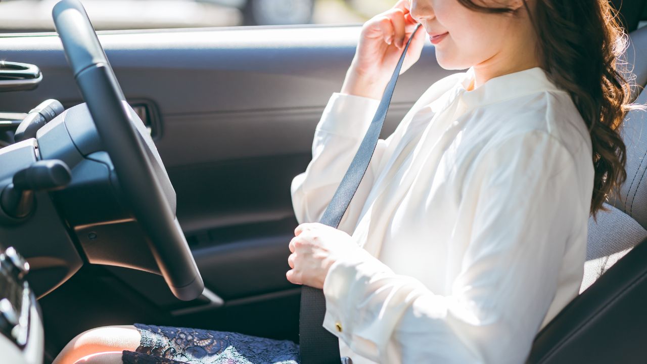 Woman waring a white blouse sitting in the driver's seat putting on seatbelt