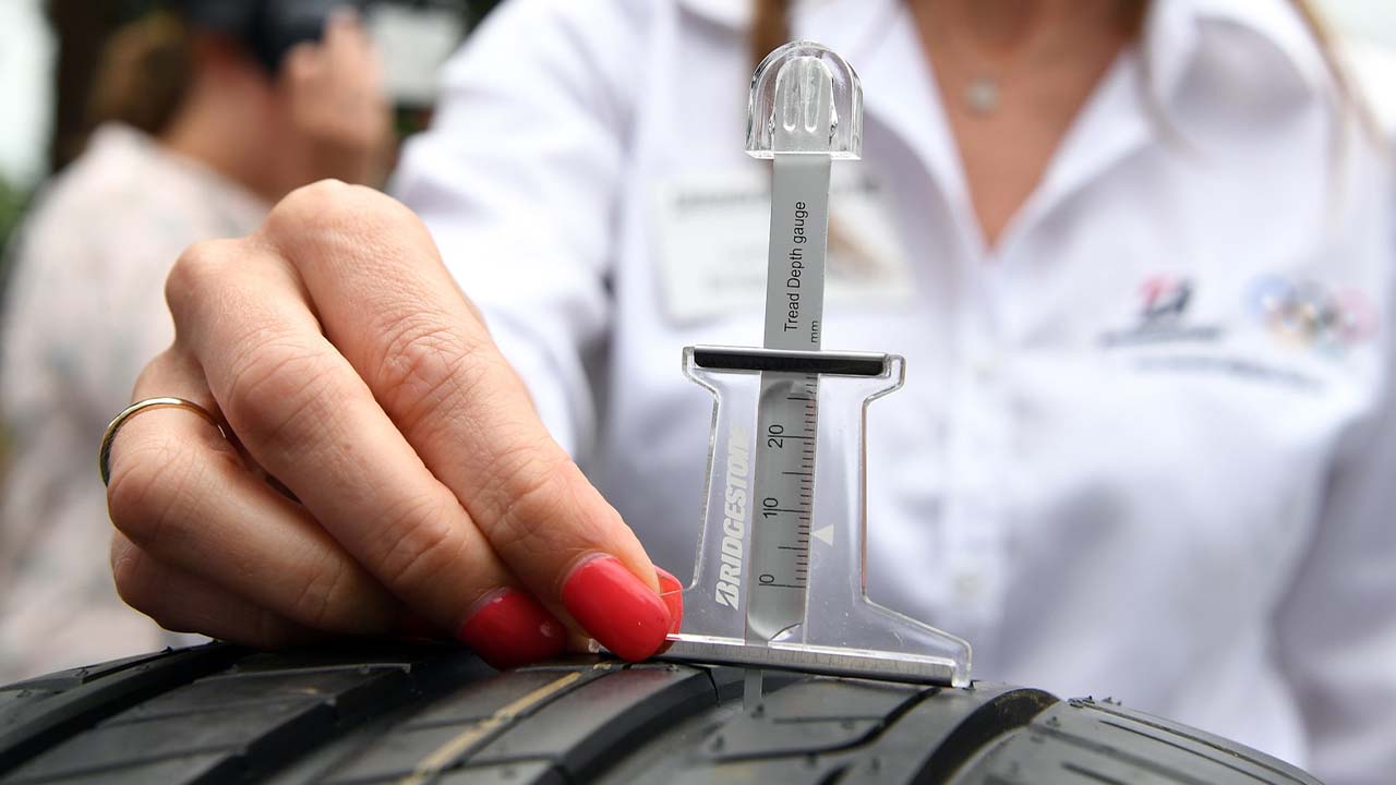 Tyre tread depth gauge being used on tyre by woman