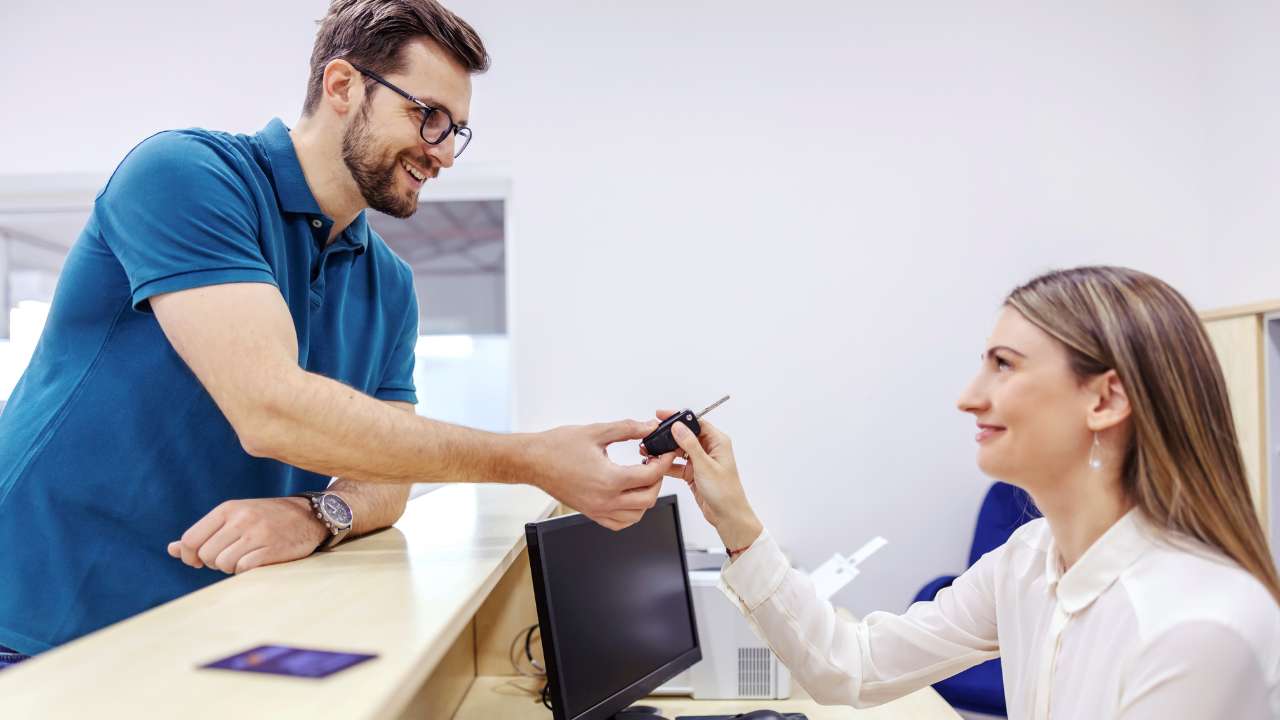 Man in blue shirt handing a car key over to a woman behind the counter