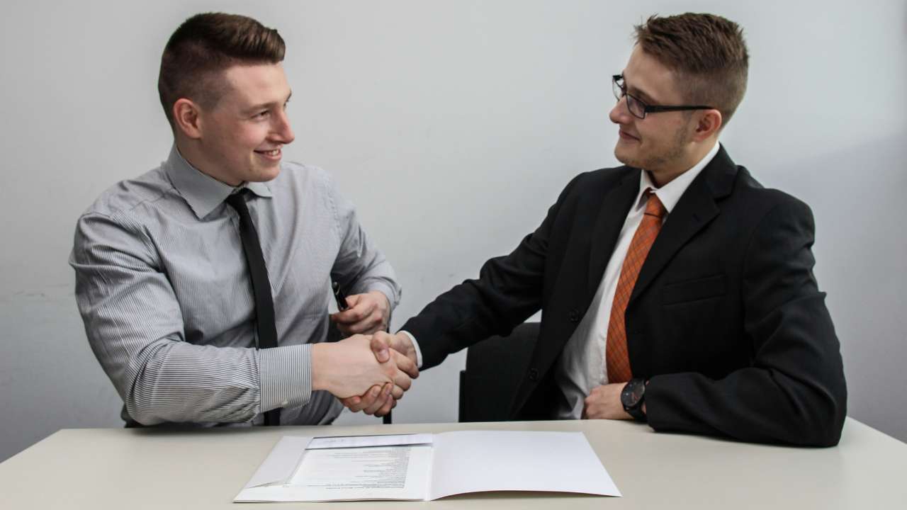 Two men shaking hands over the contract on the table