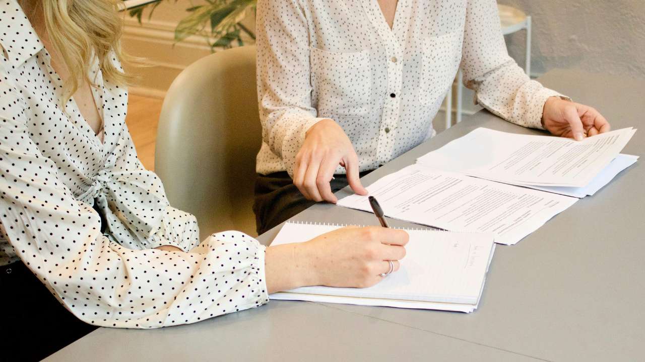 Woman signing a contract on a table with the assistance of a sales assistant