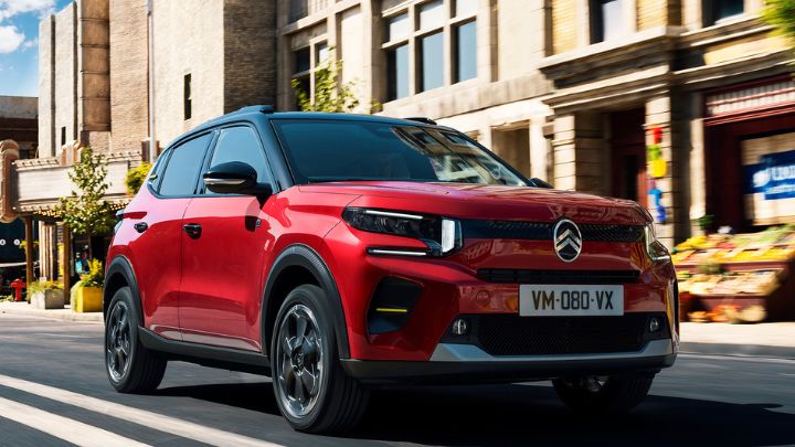 Red Citroen C3 driving on the street with shops on the side