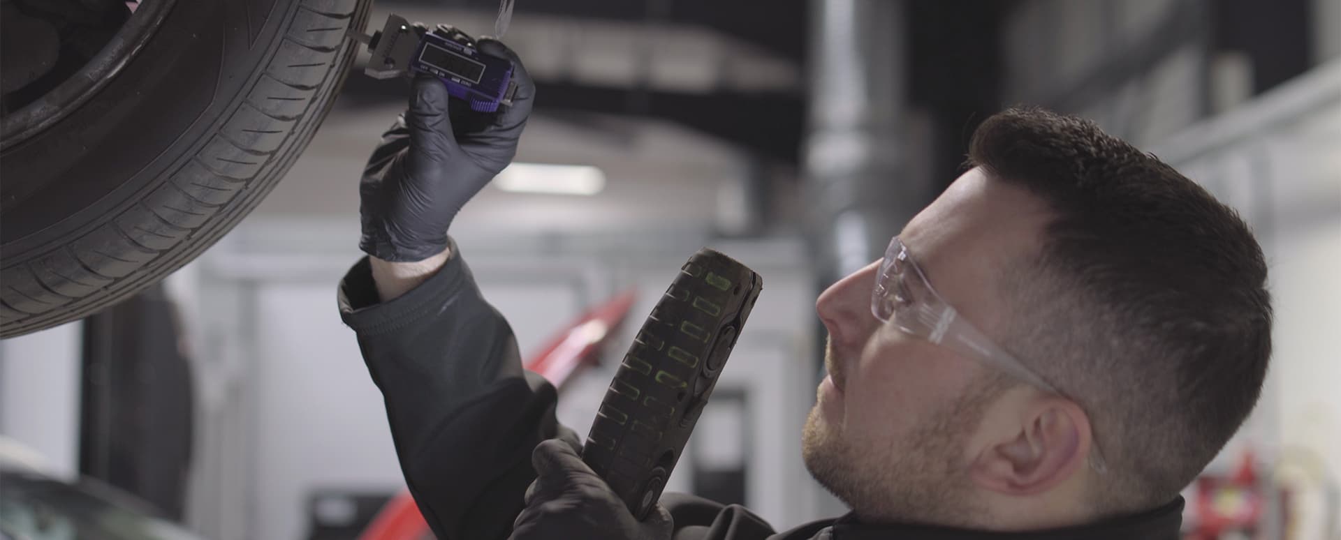 Vehicle technician checking over the tread depth of the tyre on a car