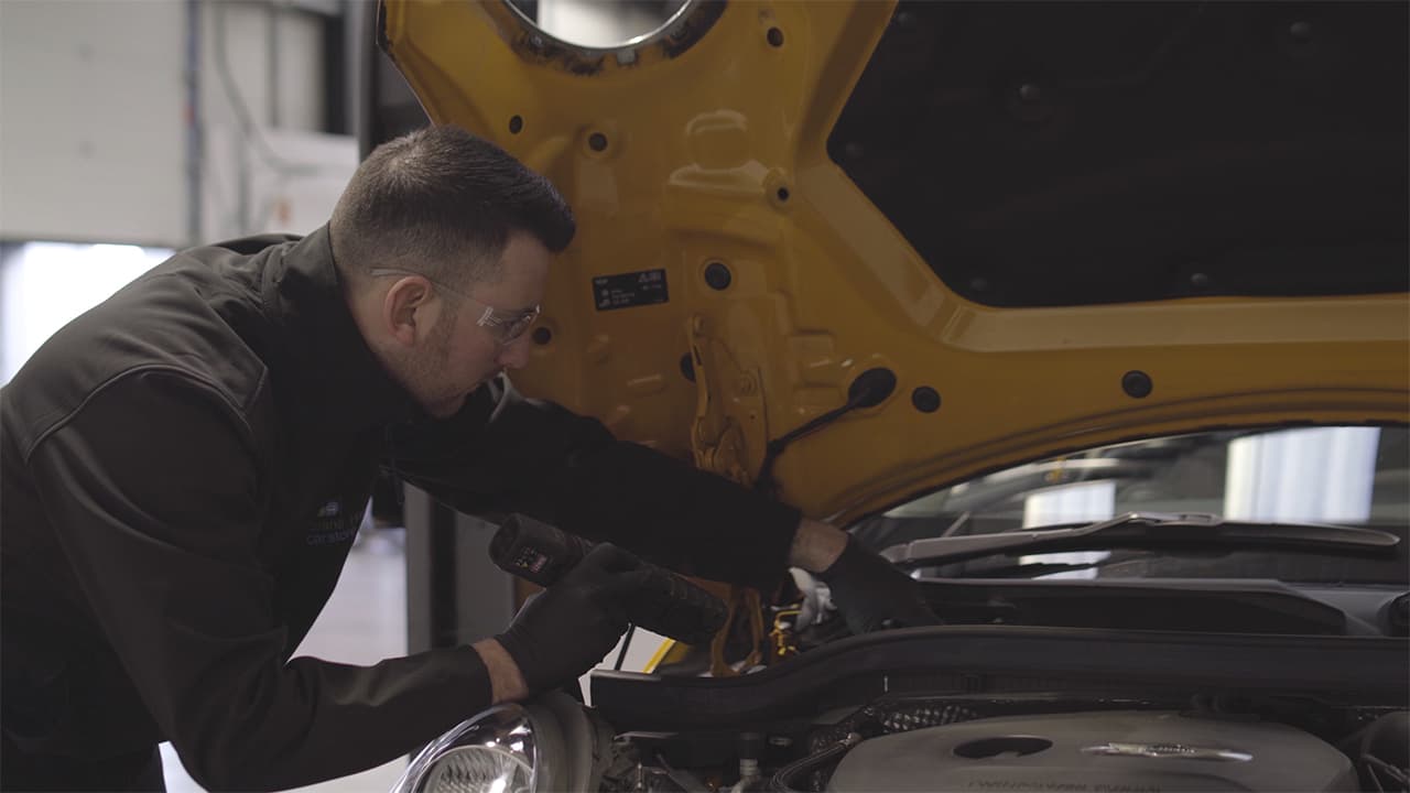 Vehicle technician checking under the bonnet of a yellow MINI Cooper