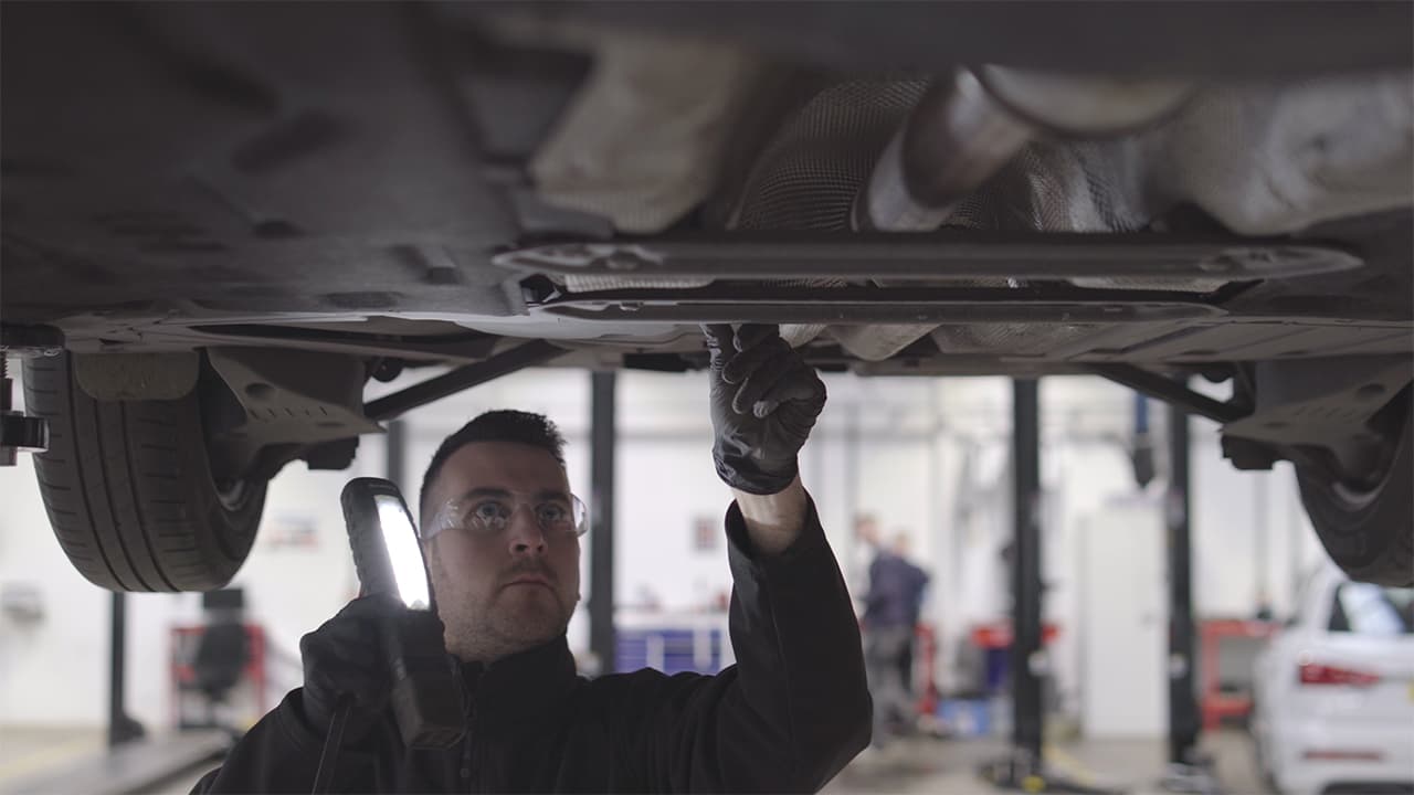 Vehicle technician checking underneath a yellow MINI Cooper