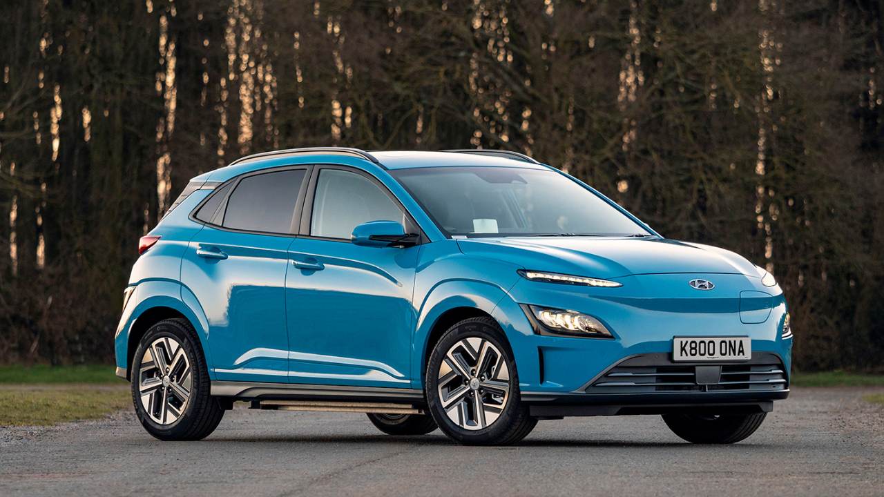 Blue Hyundai Kona parked in front of a forest with tall trees in the background
