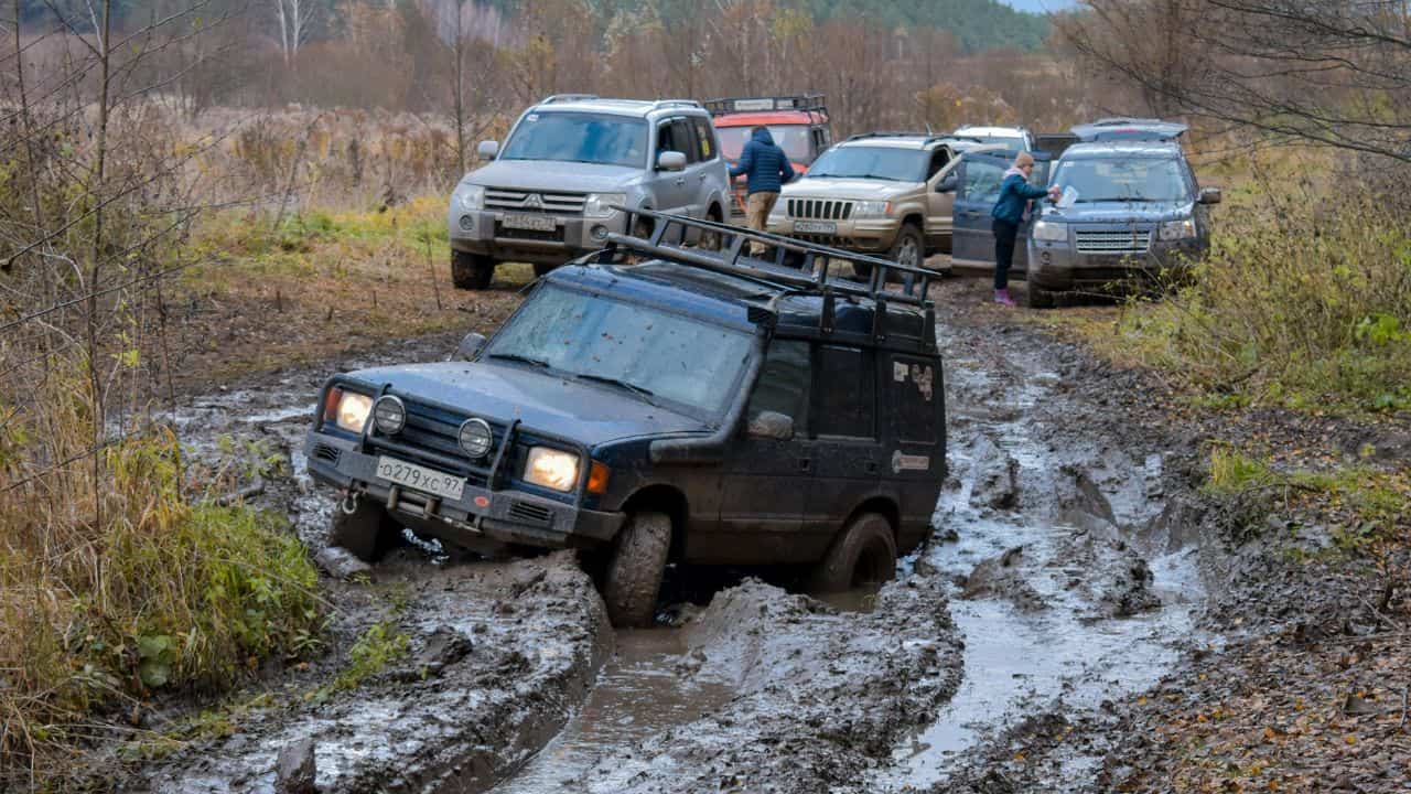 Large vehicle stuck in the mud with several other vehicles coming behind it