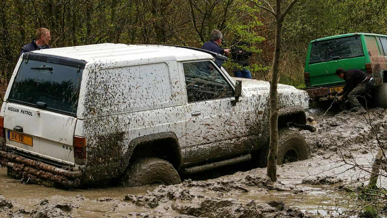 Green and white cars stuck in mud with more than half of the wheels deep into the mud puddle