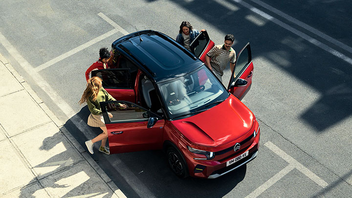 Overhead View of a Red Citroën C3 with a Black Roof. Four People are Opening the Car Doors to Get in, 