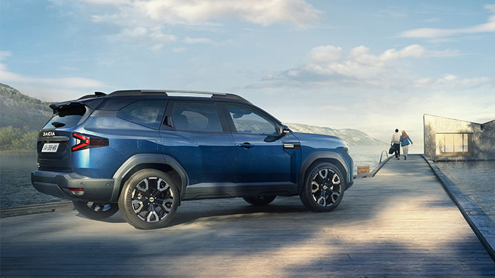 Blue Dacia Bigster On Beach With Couple Walking in Background