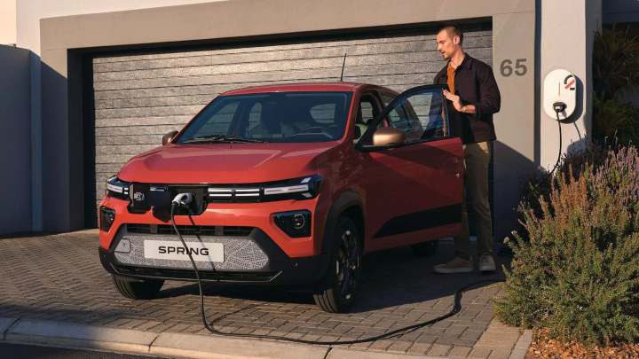 Red Dacia Spring Plugged In Charging In Front Of Home