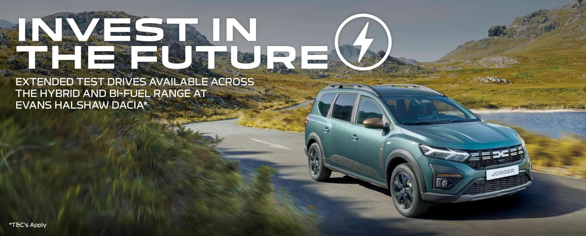 Blue Dacia SUV driving in the mountains with a beautiful lake to the right side of the car