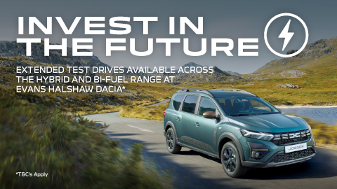 Blue Dacia SUV driving in the mountains with a beautiful lake to the right side of the car