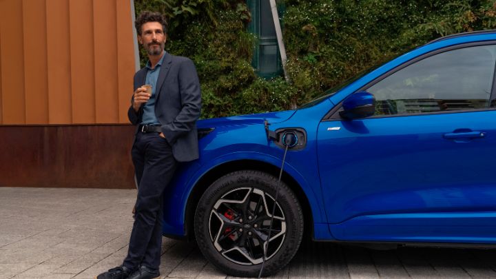 Man standing next to his blue Ford Kuga whilst its being charged