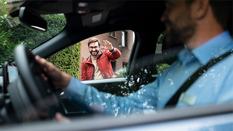 Ford customer waving through the window of a car to a Ford employee driving off
