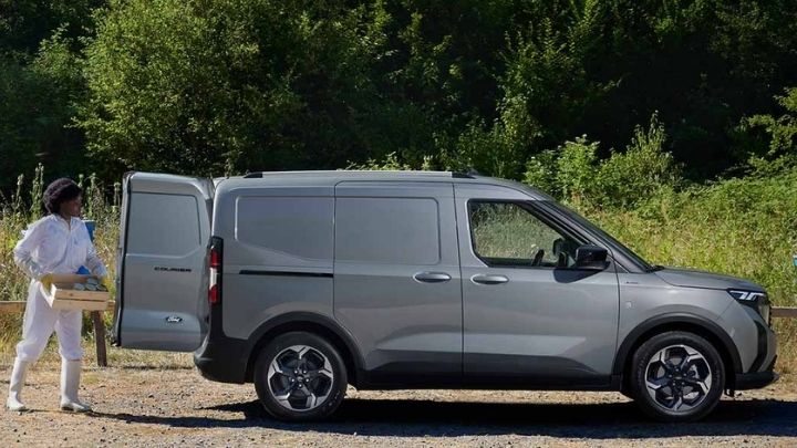 Silver Ford E-Transit Courier with the back doors open and a man carrying a box to the boot